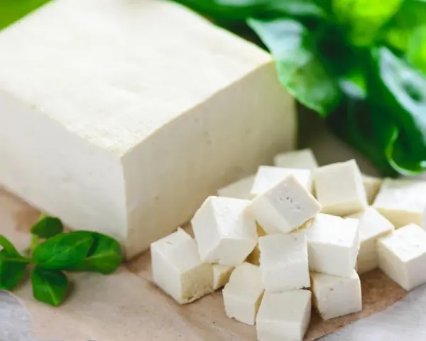 Kostka i pokrojone w kostkę tofu, obok zielone listki. Tak wygląda tofu – białe, delikatne, gotowe do przygotowania.