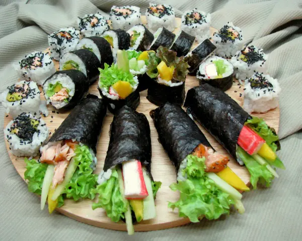Talerz sushi z futomaki i uramaki. Widać rolki z łososiem, awokado, sałatą, paluszkami krabowymi i mango.