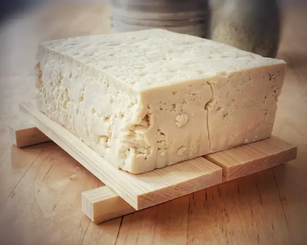 Duży blok domowego tofu na drewnianej podstawce, gotowy do przygotowania pysznych dań.