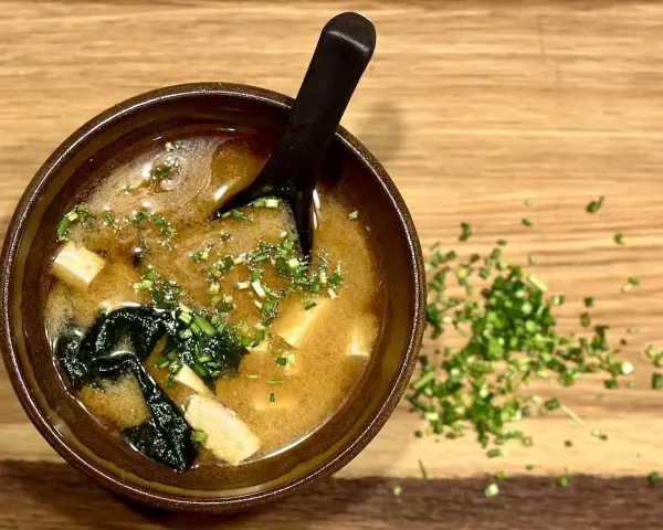 Miseczka aromatycznego miso shiru z tofu i wodorostami, posypana szczypiorkiem.
