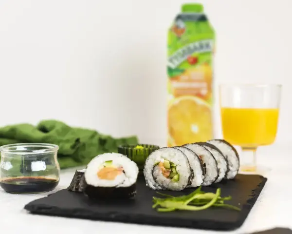 Pyszne sushi z łososiem, ogórkiem i ryżem, podane z sosem sojowym i sokiem pomarańczowym.