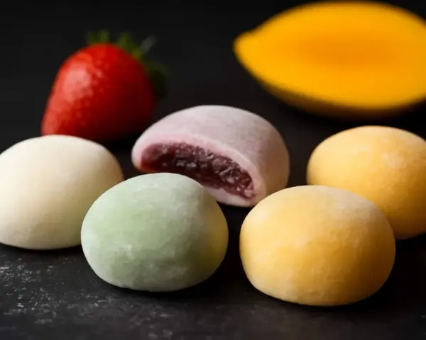 Kolorowe mochi, jak jeść? Delikatne kuleczki z nadzieniem, obok truskawka i mango.