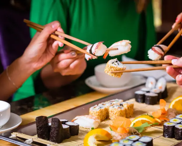 Ręce trzymają pałeczki, jedząc sushi. To smakowita uczta, która odzwierciedla japońskie tradycje kulinarne.