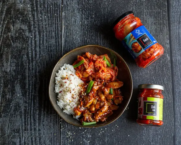 Miseczka ryżu z kurczakiem w sosie i kimchi, obok słoiczki z kimchi i pastą chili.