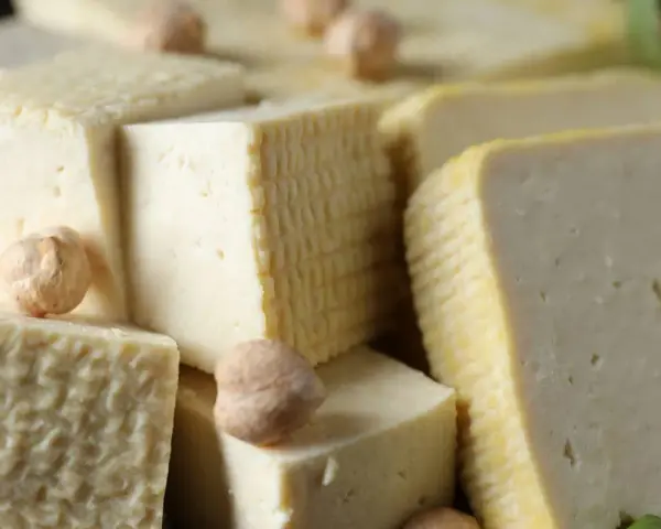 Kawałki miękkiego tofu ułożone obok siebie, niektóre z nich mają kratkowaną fakturę. Kilka ciecierzycy dodaje uroku.