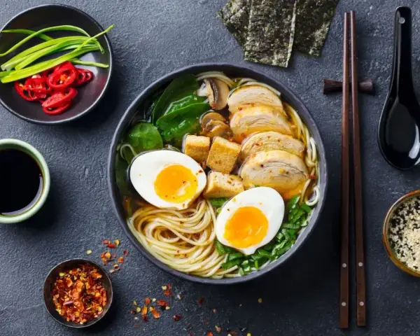 A miseczce aromatycznego ramenu z tofu, jajkiem na pół, kurczakiem i zieloną cebulką. Obok sos sojowy, chili i nori.