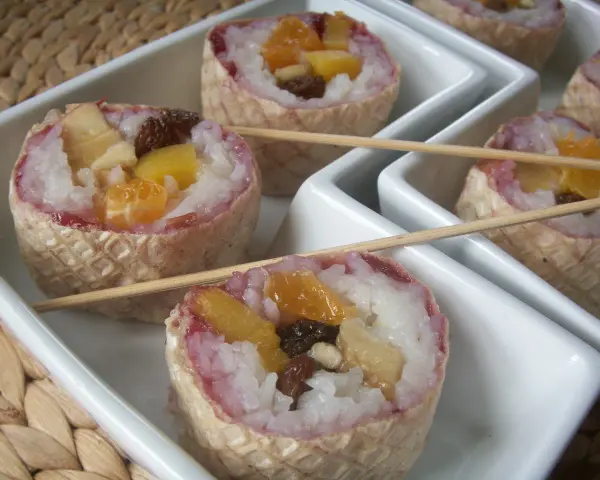 Słodkie sushi owocowe w wafelkach, z ryżem i kawałkami owoców, podane na białych tacach.
