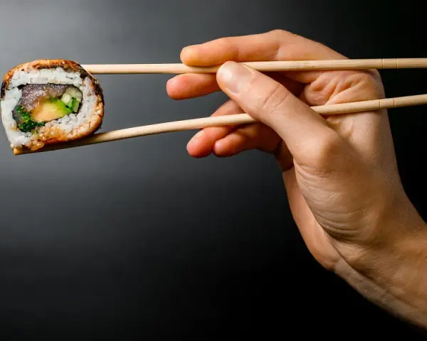 Dłoń trzyma pałeczkami jedno sushi. Zastanawiasz się, ile sushi na osobę będzie idealne na kolację?