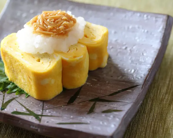 Roladki tamago z tartą rzodkwią i grzybami enoki na talerzu z motywem bambusa.