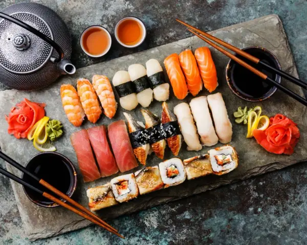 Piękne składniki na sushi: nigiri z łososiem, krewetkami, tuńczykiem, węgorzem i rybą maślaną, a także rolki. Obok czajniczek, sos sojowy i marynowany imbir.