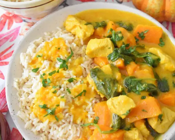 Aromatyczny kurczak curry z dynią i mlekiem kokosowym, podany z ryżem i posypany natką pietruszki.