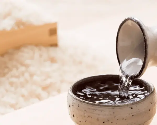 Sake przelewana z dzbanka do czarki, w tle ryż. Poznaj, jak smakuje sake.