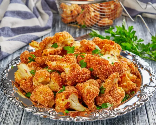Chrupiący kalafior w panko, podany na ozdobnej tacy, posypany świeżą natką pietruszki. Idealna przekąska!