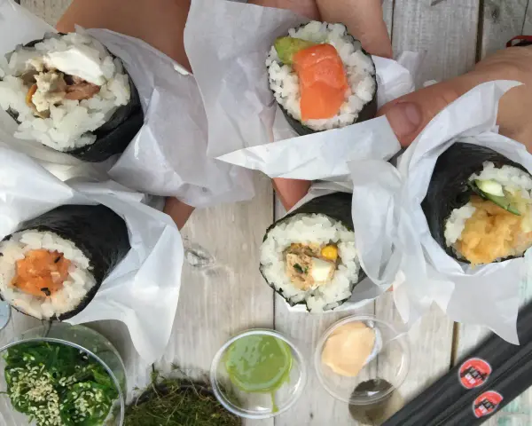 Ręcznie robione handroll sushi z łososiem, awokado, tuńczykiem i krewetkami. Pyszne przekąski na drewnianym stole.