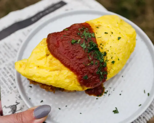 Pyszny omlet ryżowy polany sosem pomidorowym i posypany natką pietruszki, podany na talerzu.