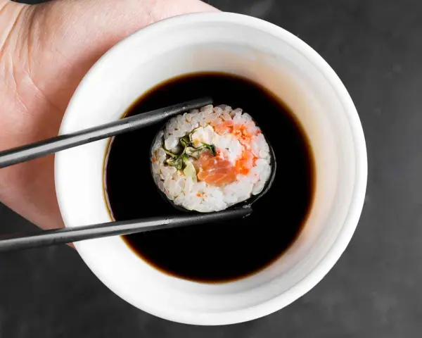 Pałeczkami zanurzam rolkę sushi w ciemnym sosie. Idealny sos słodki do sushi podkreśla smak ryby i ryżu.