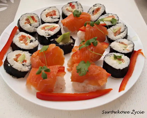 Piękne sushi kompozycje na białym talerzu: rolki z łososiem, awokado i papryką, ozdobione kolendrą.