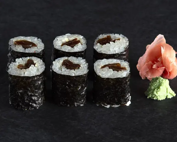 Sześć roladek sushi z ryżem i ciemnym nadzieniem, prawdopodobnie sushi z tykwą. Obok różowy imbir i zielone wasabi.
