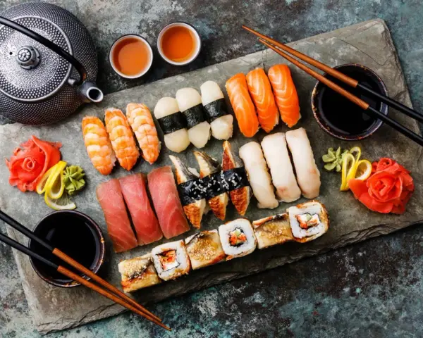 Zestaw sushi: nigiri z łososiem, krewetkami, tuńczykiem, węgorzem i rolki. Obok czajniczek, miseczki z herbatą i sos sojowy. Tak jedzą japończycy.