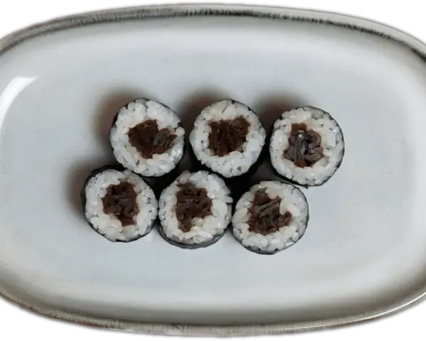 Sześć kawałków sushi z ryżem i ciemnym nadzieniem na szarej tacy.