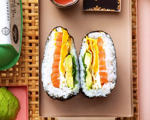 Dwa połówki onigiri z łososiem, awokado i jajkiem, podane na talerzu z pałeczkami.