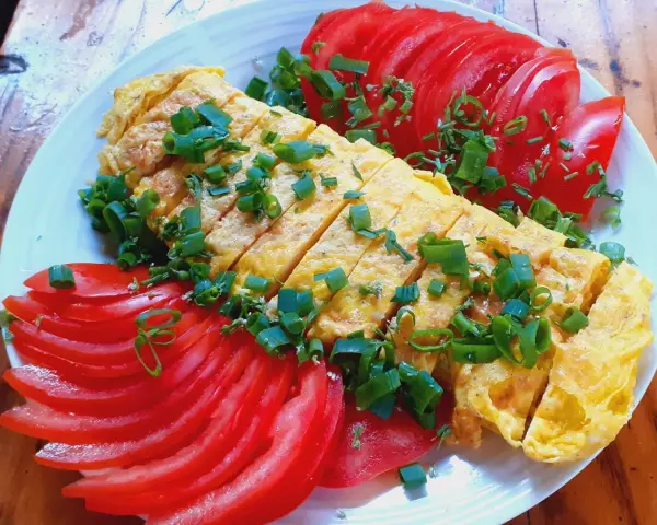 Pyszne koreańskie śniadanie: pokrojony omlet z jajek posypany szczypiorkiem, podany z plasterkami pomidora.