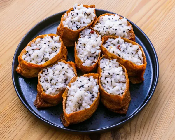 Tofu inari z ryżem i czarnym sezamem na czarnym talerzu.