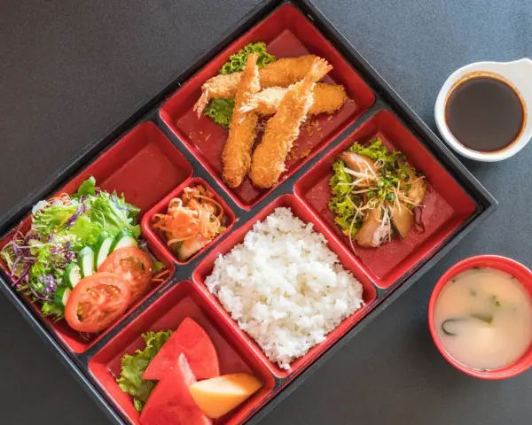Japoński obiad w bento: smażone krewetki, ryż, sałatka, owoce i zupa miso.
