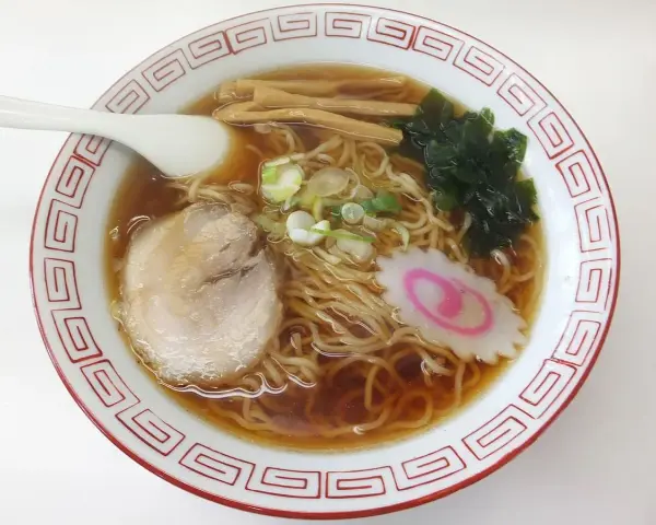 Miseczka aromatycznego ramenu, dania, którego **ramen skąd pochodzi** jest z Japonii. Widać makaron, plastry mięsa, nori, bambus i narutomaki.