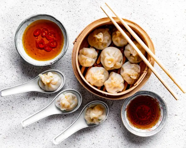 Pyszne dim sum w bambusowym parowniku, podane z sosem chili i sosem sojowym. Trzy pierożki na łyżeczkach zachęcają do spróbowania.