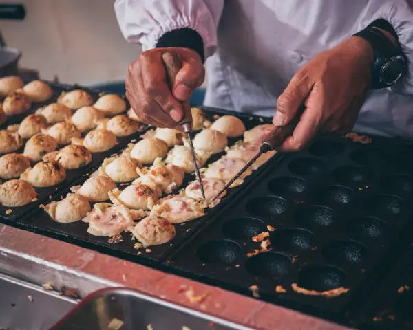 Ręce obracają kulki takoyaki na specjalnej patelni. Ten prosty takoyaki przepis jest w trakcie realizacji.