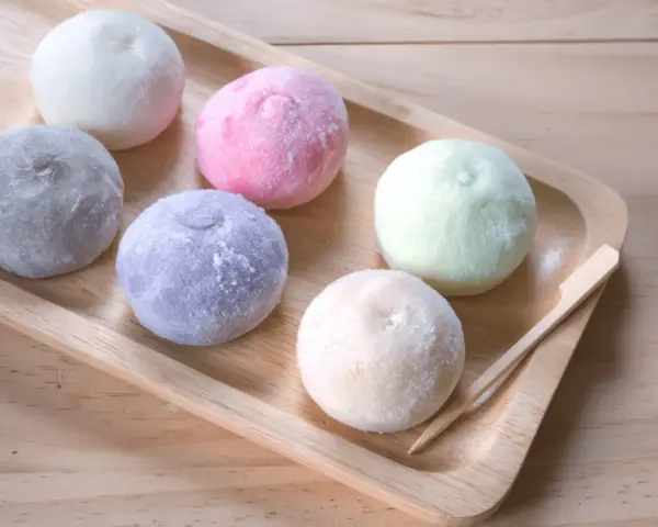 Kolorowe desery azjatyckie, mochi, ułożone na drewnianej tacy.