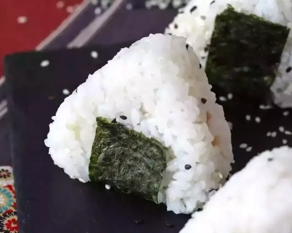 Trójkątne onigiri z tuńczykiem, ryżem i wodorostami nori, posypane sezamem.