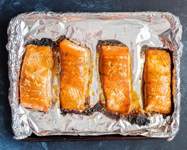 Cztery kawałki pieczonego łososia na folii aluminiowej. Idealny łosoś do sushi, lekko przypieczony na brzegach, zachęca do przygotowania.
