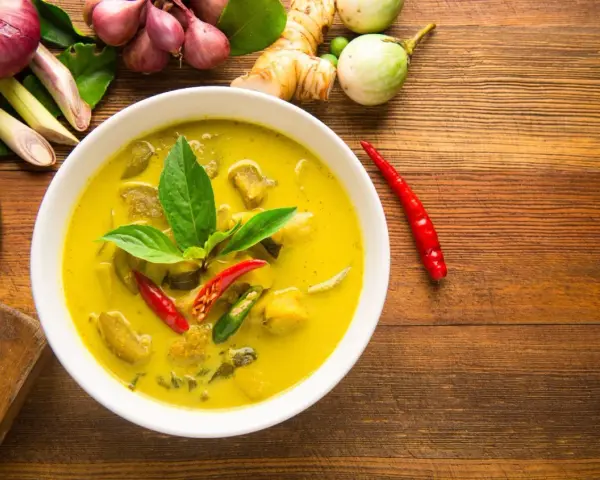 Aksamitne tajskie curry z tofu, ozdobione świeżą bazylią i papryczkami chili, otoczone składnikami jak galangal i trawa cytrynowa.