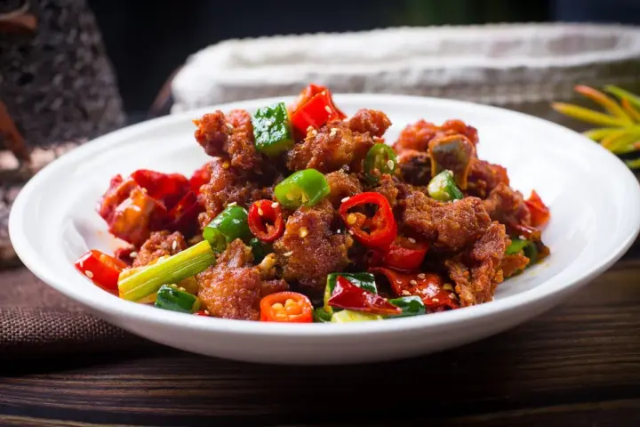 Chrupiący kurczak po kantonsku z papryczkami chili i zieloną cebulką na białym talerzu.