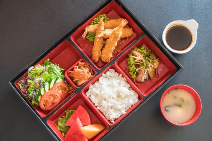 Japoński obiad w bento: smażone krewetki, ryż, sałatka, owoce i zupa miso.
