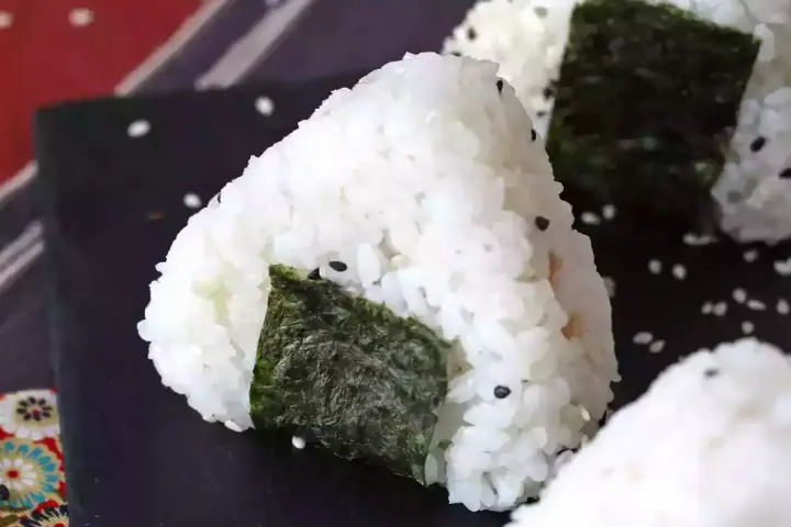 Trójkątne onigiri z tuńczykiem, ryżem i wodorostami nori, posypane sezamem.