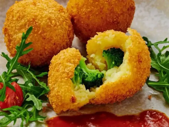 Chrupiące kulki ziemniaczane w panko z brokułami w środku, podane z rukolą i pomidorkami.