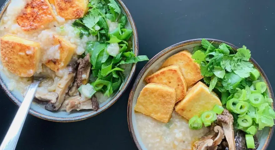 Dwie miseczki aromatycznego congee z chrupiącym tofu, grzybami i świeżymi ziołami.