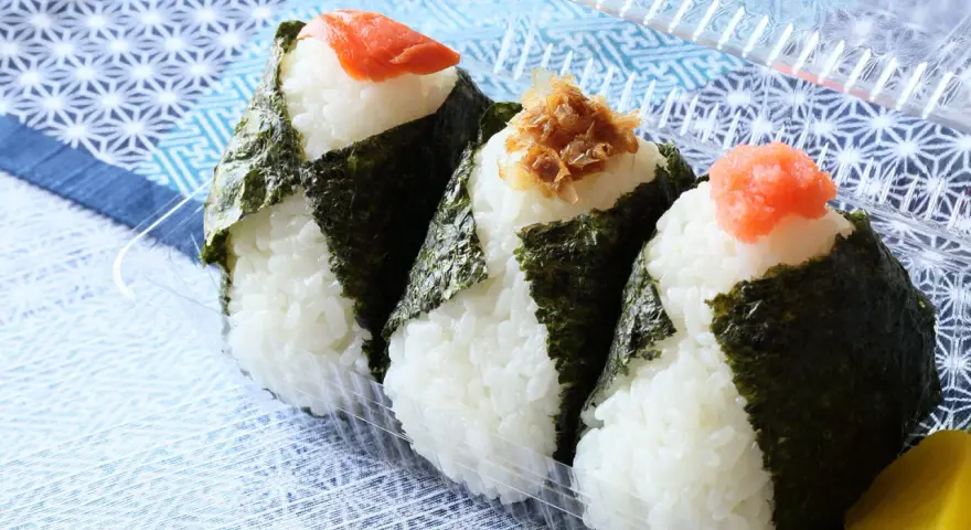 Trzy onigiri z ryżem, zawinięte w nori, z łososiem, tuńczykiem i ikrą na wierzchu. Idealne na przekąskę.