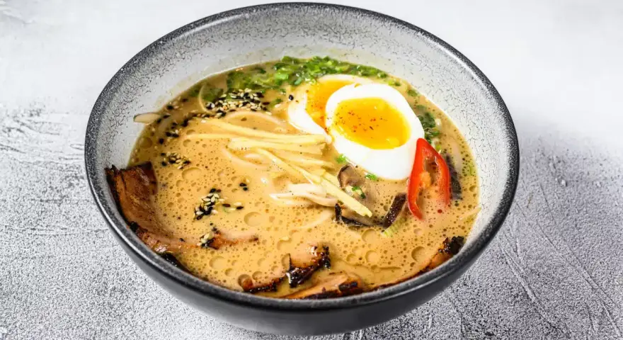 Miseczka aromatycznej zupy ramen z jajkiem na pół, plastrami mięsa, grzybami i szczypiorkiem.
