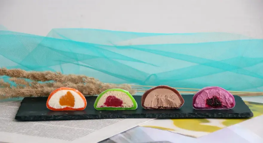 Cztery kolorowe mochi: pomarańczowe, zielone z malinami, czekoladowe i fioletowe z jagodami. Różne rodzaje słodkości.