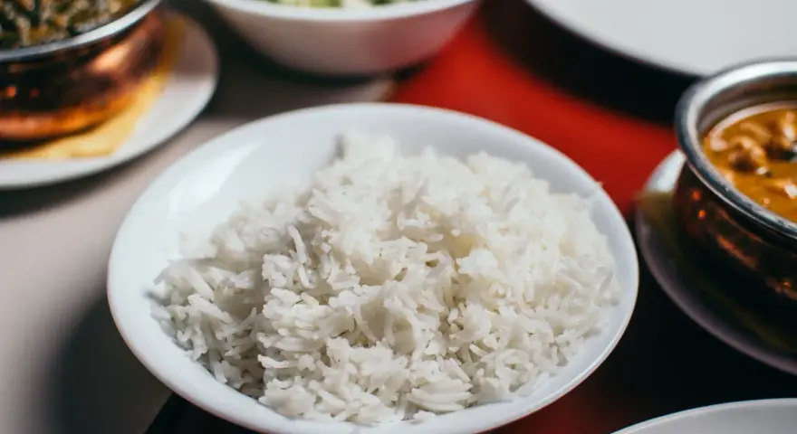 Biały ryż w misce, który jest głównym źródłem węglowodanów w wielu kuchniach. Obok dania curry i sałatka.