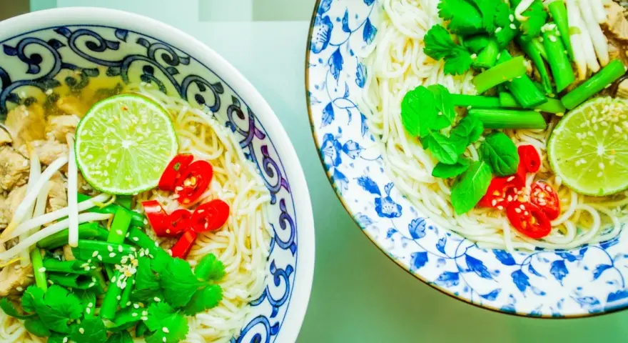 Dwie miseczki aromatycznej zupy pho z makaronem, mięsem, kiełkami, limonką, chili i świeżymi ziołami.