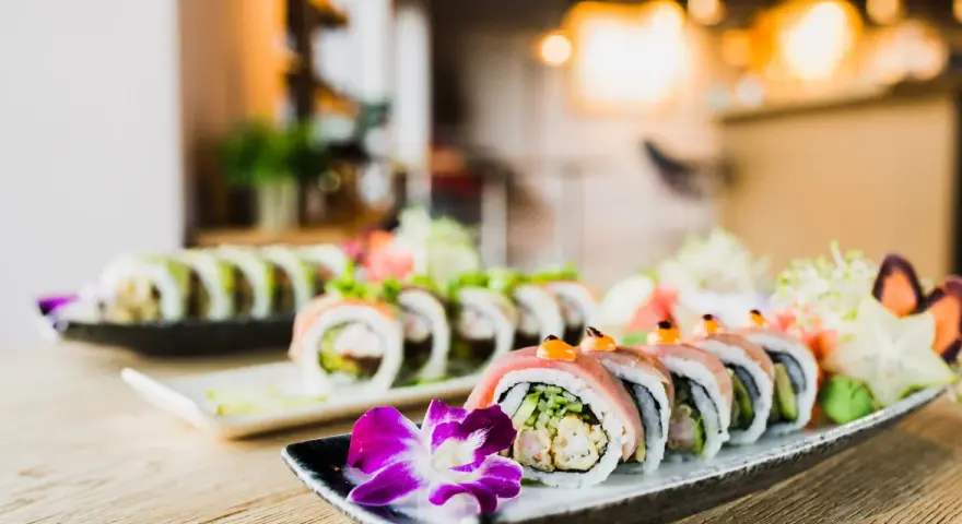 Wykwintne sushi z mięsem, ozdobione kwiatem i warzywami, prezentuje się apetycznie na talerzu.