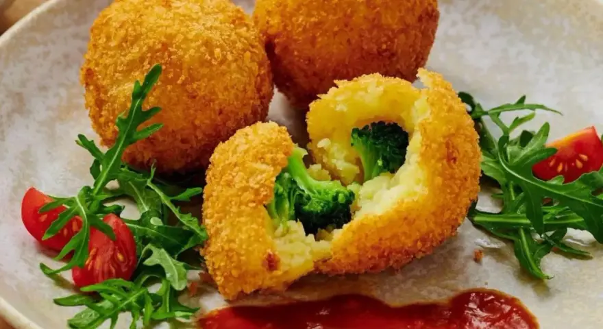 Chrupiące kulki ziemniaczane w panko z brokułami w środku, podane z rukolą i pomidorkami.