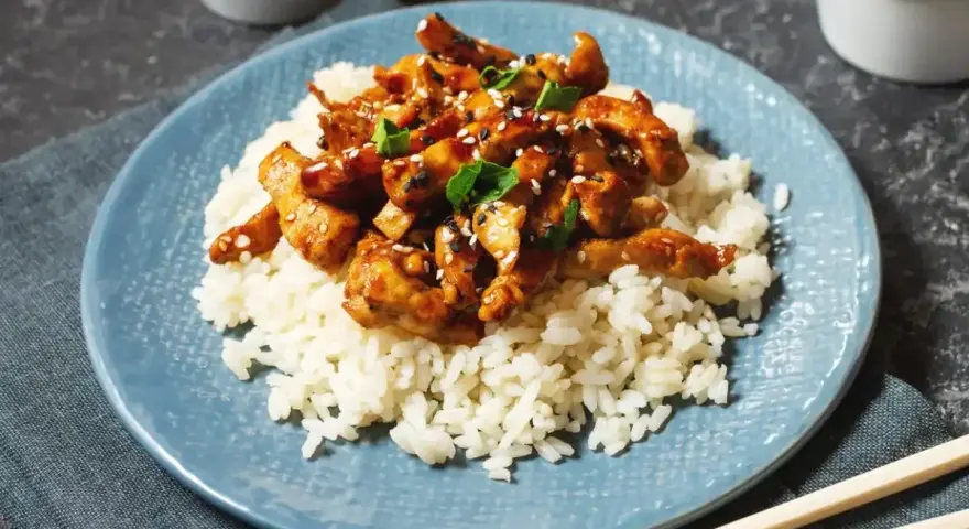 Pyszny kurczak po japońsku w sosie teriyaki, podany na ryżu z sezamem i szczypiorkiem. Idealny posiłek dla miłośników azjatyckich smaków.