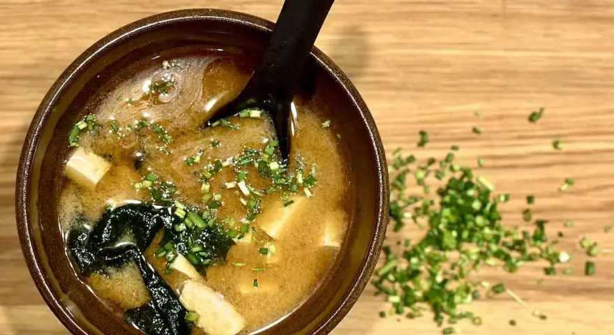 Miseczka aromatycznego miso shiru z tofu i wodorostami, posypana szczypiorkiem.