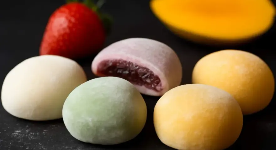 Kolorowe mochi, jak jeść? Delikatne kuleczki z nadzieniem, obok truskawka i mango.